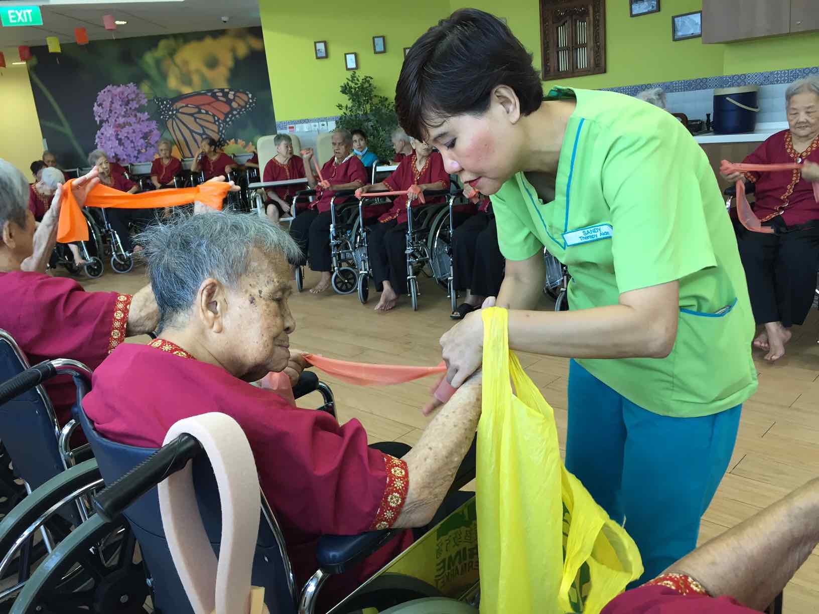 sandy-helping-elderly-tie-their-therabands-at-ntuc-health-nursing-home-aspirantsg